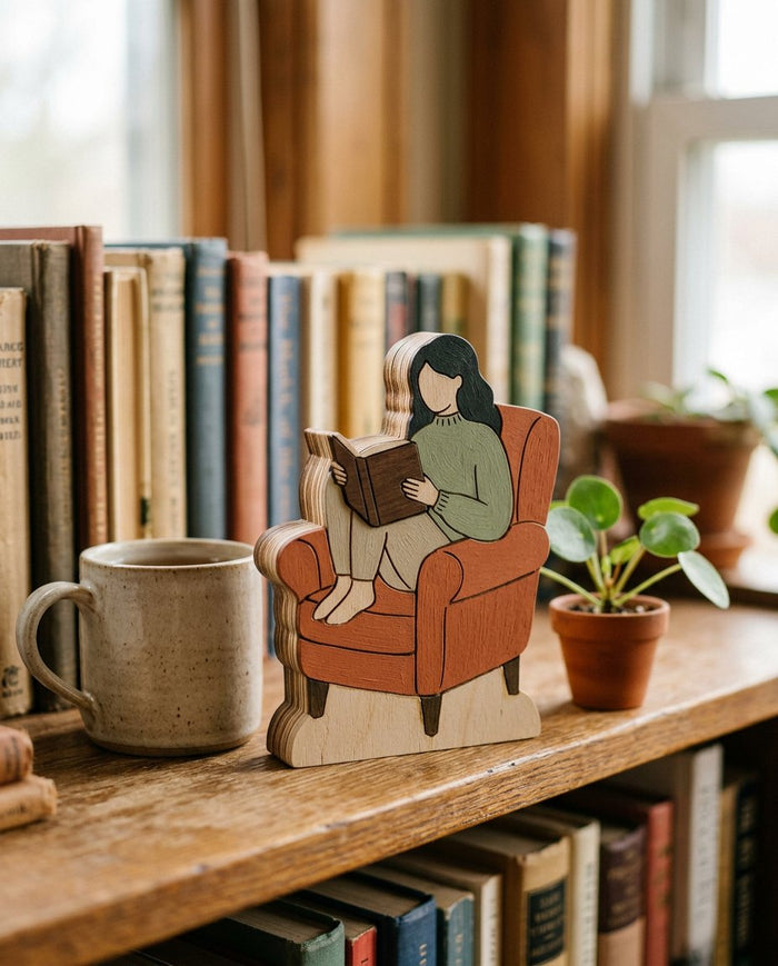 Wooden standing figure of a woman reading in an armchair on a bookshelf
